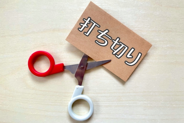 「打ち切り」と書かれた紙をはさみで切っている