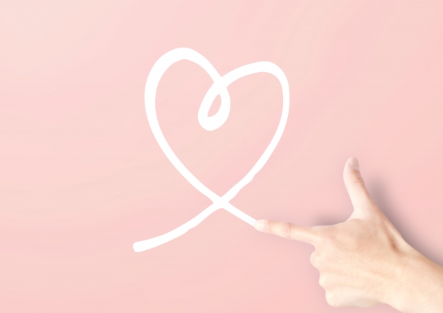 ピンクの背景に、指でハートを描いている