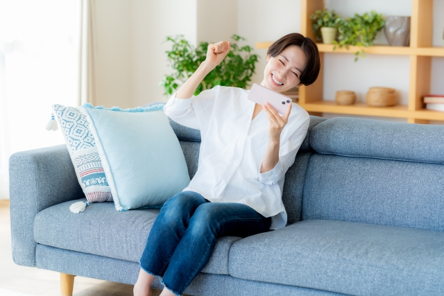 部屋でスマホを操作するミドル女性