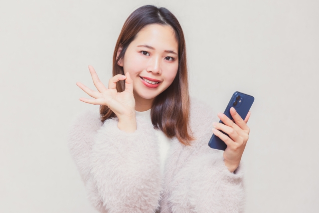 女性がスマホ片手にGOODサイン